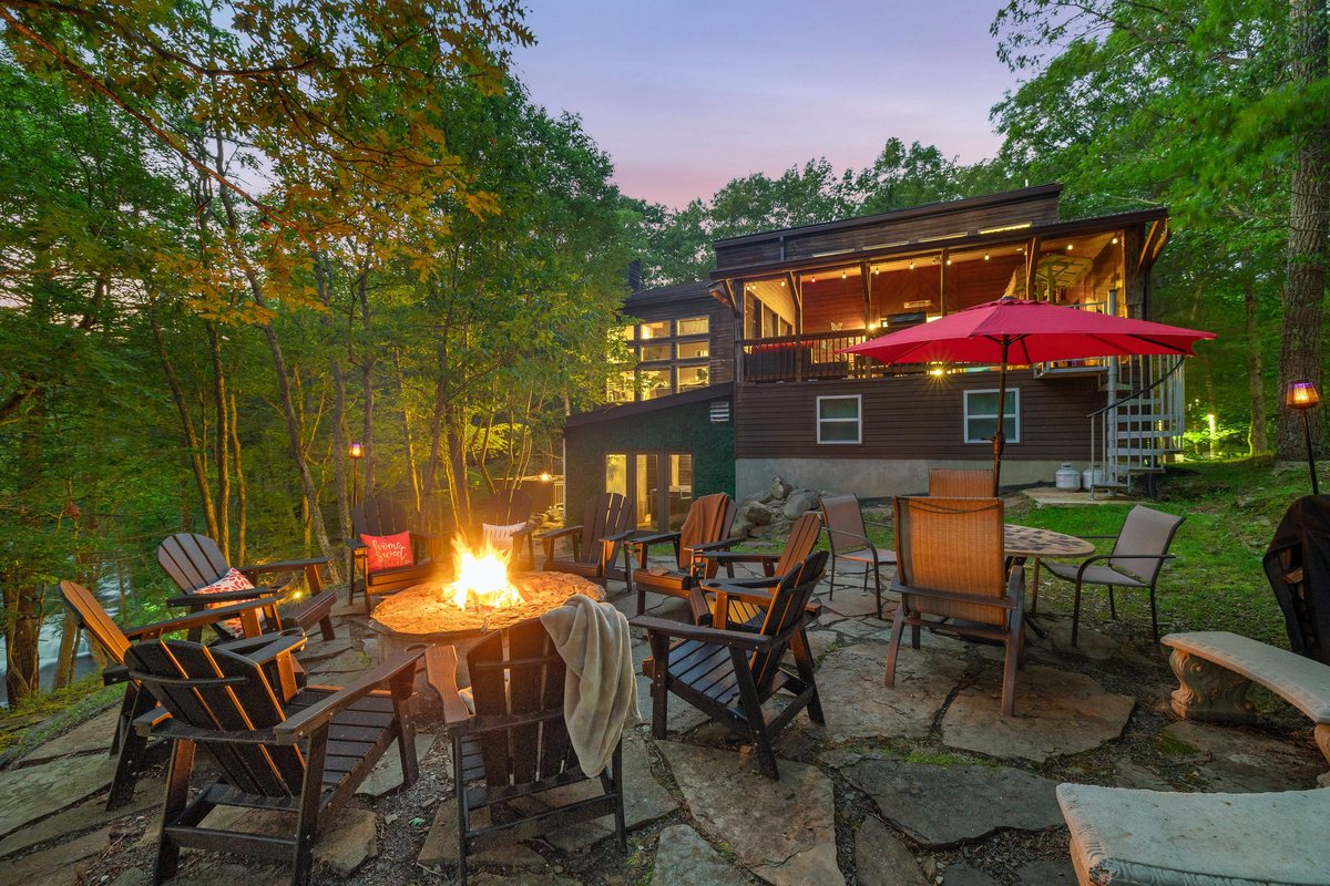 Fire pit glowing at dusk with Waterfall Wonder lit behind it in the forest.